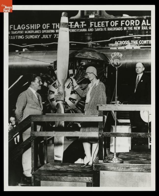 Ameia Earhart holds a bottle of champagne at the front of an airplane