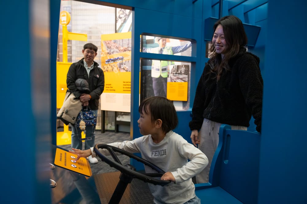 A child plays in a fake city bus while her parents watch