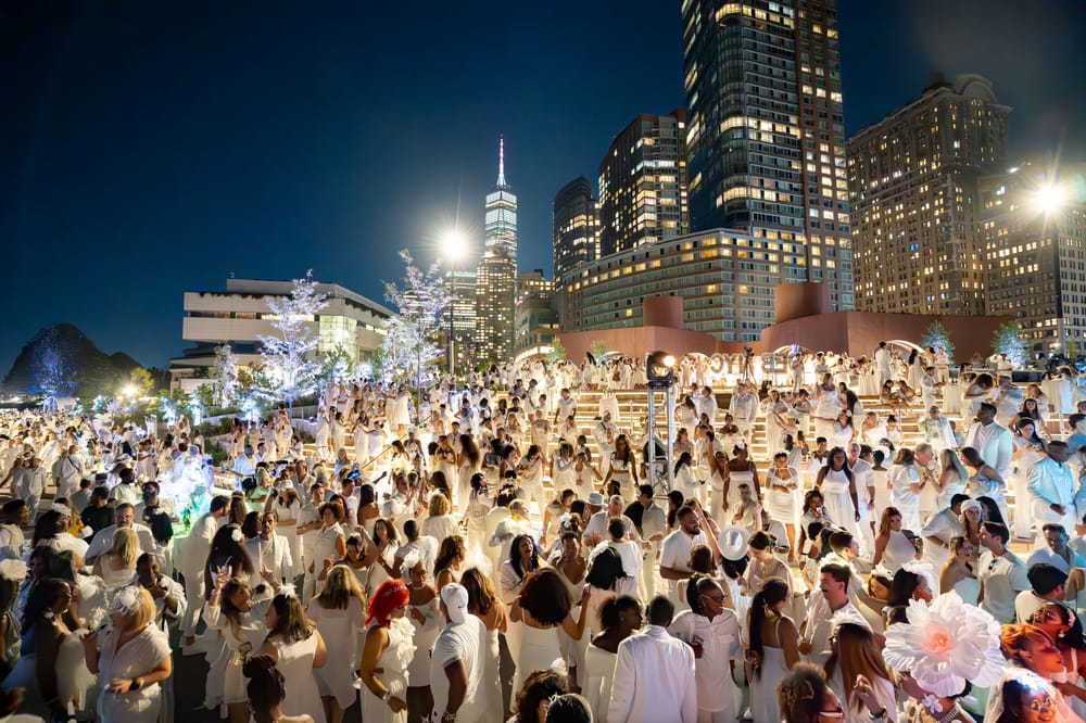 A crowd of diners dressed in white set against the backdrop of the lower Manhattan skyline