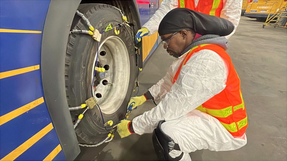 A man puts snow chains on a bus tire