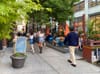People walking on a sidewalk past a curbside dining set up