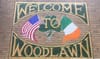 "Welcome to Woodlawn" painted sign on a brick wall with Irish and American flag